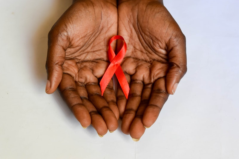 African dark brown skin cupped hands holding red ribbon for HIV AIDS