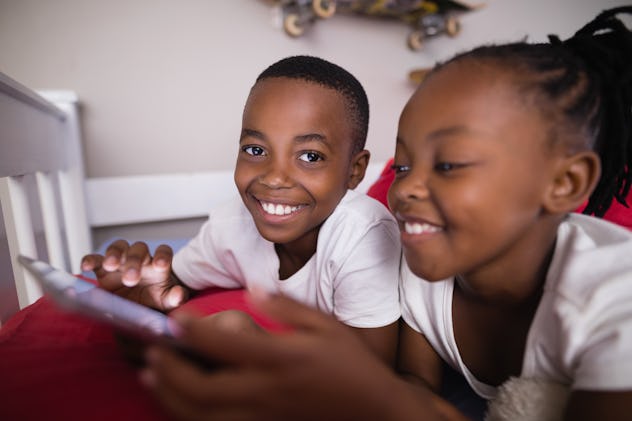 Close up of happy siblings using mobile phone while lying on bed at home