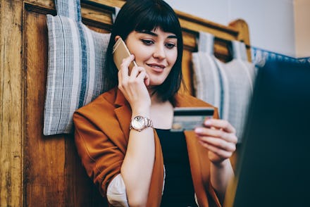 Positive woman looking at number on credit card and confirm purchase via telephone call to customer ...