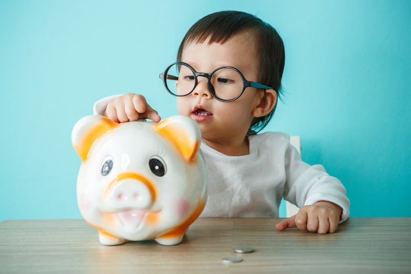 Baby child putting a coin into a piggy bank, kid saving money for future concept