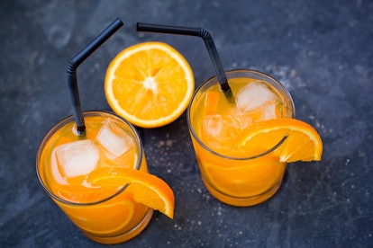 two glasses with an orange drink and an orange slice  with tubules on a dark concrete background clo...