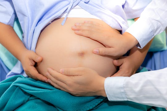 Handsome doctor is checking fetal position by touching pregnant woman belly at hospital. Beautiful m...