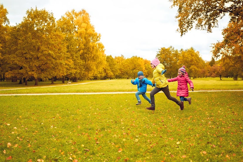 autumn, childhood, leisure and people concept - group of happy little kids playing tag game and runn...