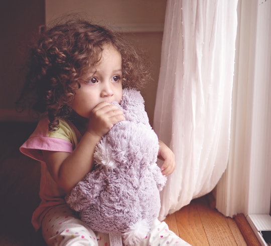 Toddler girl with curly hair sitting by a window with her stuffed animal.