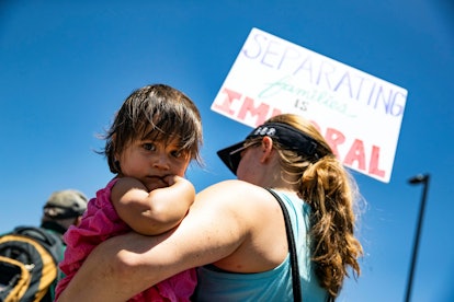 A demonstrator holds her child and a poster reading 'Separating Families is Immoral' in front of the...