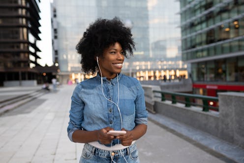 attractive happy dark skinned girl is listening to music with headphones looking at a mobile phone a...