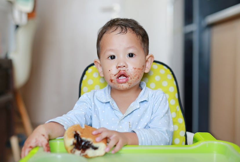 Asian little baby boy sitting on children chair indoor eating bread with Stuffed Chocolate-filled de...