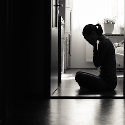 Silhouette of sad woman covering face sitting at home in a dark room. 