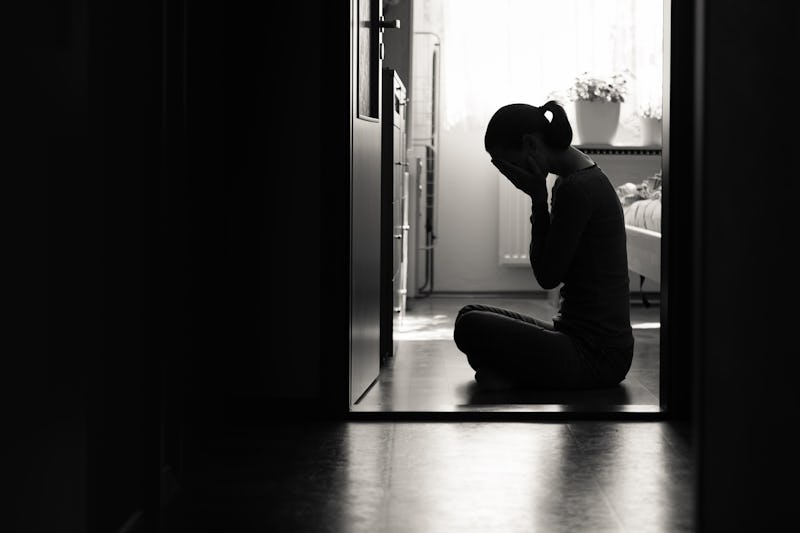 Silhouette of sad woman covering face sitting at home in a dark room. 