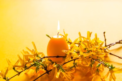 Yellow candle in the shape of egg and beautiful spring forsythia plant branches. Easter decor elemen...
