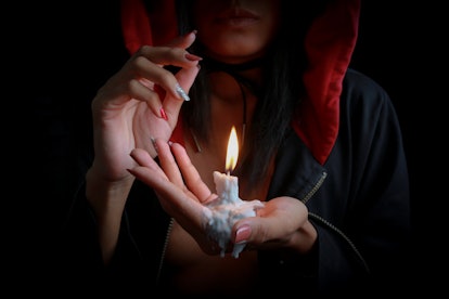 Sexy girl in witch hoodie holding melted candle. Look like super natural have magic to make a wishes...