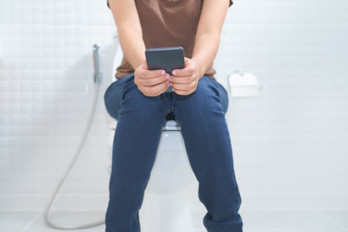 Woman sitting on toilet and using smartphone - constipation concept.