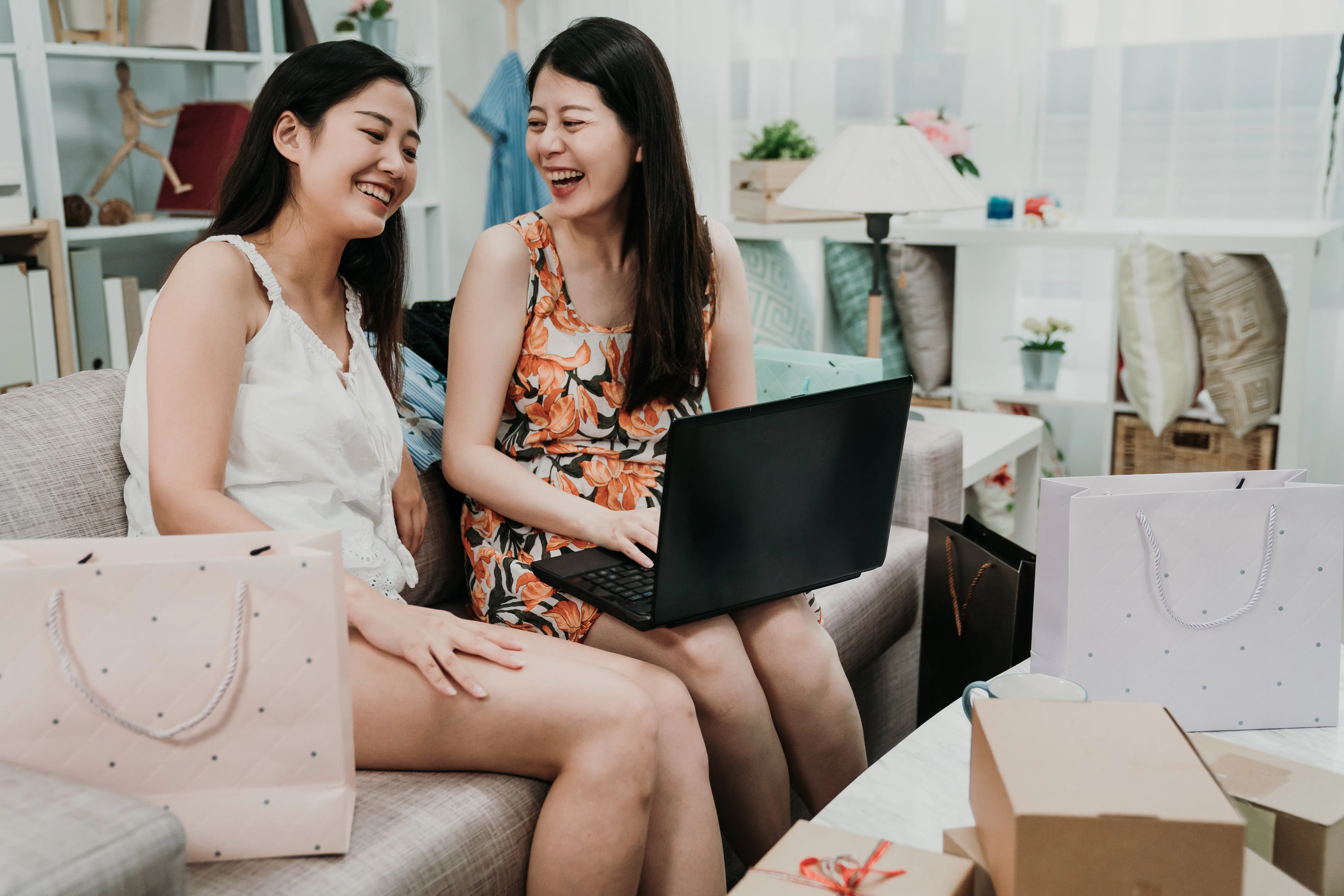 two young girls best friends sitting on couch sofa in living room with cardboards and boxes bags all...