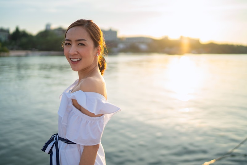 Asian beautiful girl smiling happy on sunset sea vacation enjoying warm sunshine. Mixed race Asian C...
