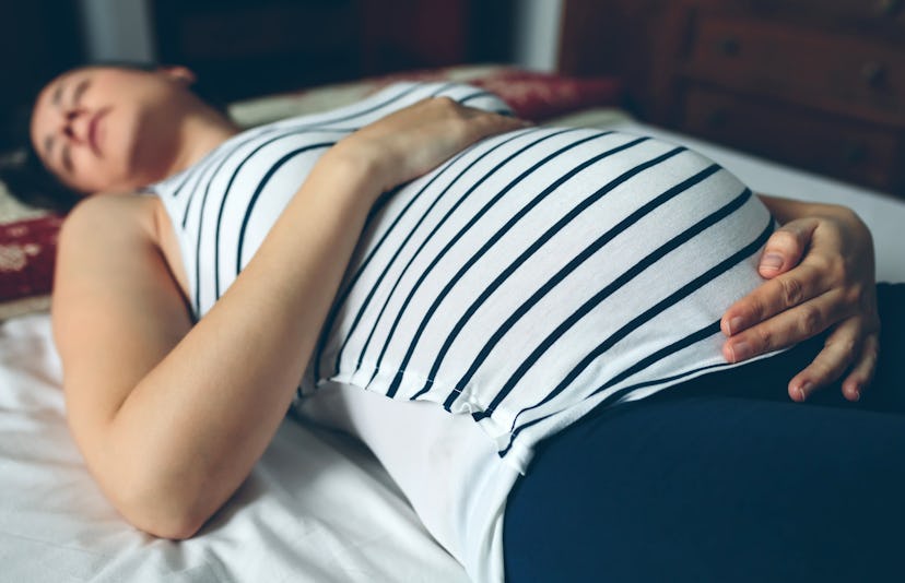 Pregnant woman sleeping in bed and touching her belly