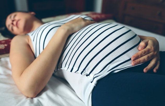 Pregnant woman sleeping in bed and touching her belly.