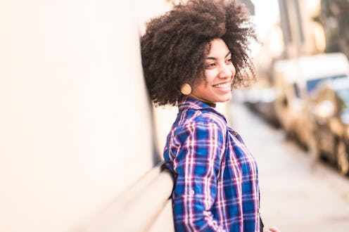 Happy and cheerful young mixed race girl smiling in the city with cars parked in background - bright...