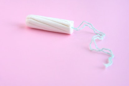 One white tampon with selective focus and empty space for text or image on blurred pink background. ...