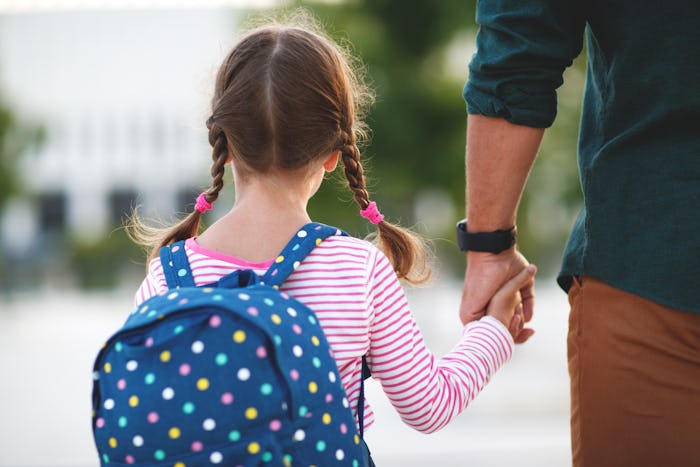 first day at school. father leads a little child school girl in first grade
