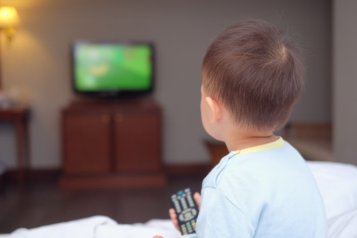 Cute little Asian 2-3 years old toddler baby boy child sitting in bed holding the tv remote control ...
