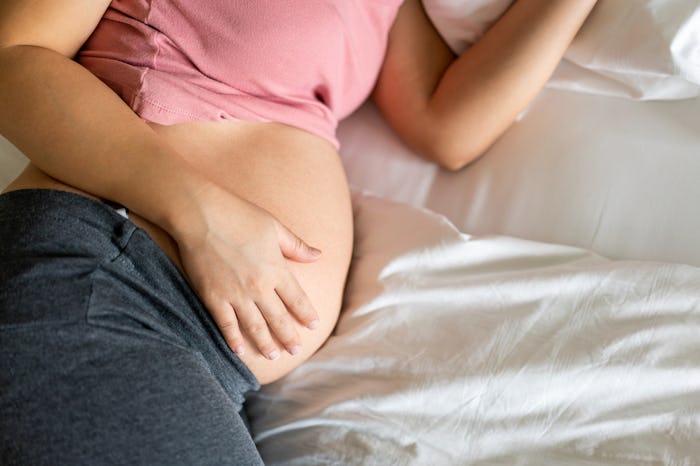 Pregnant woman feeling happy at home while taking care of her child. The young expecting mother hold...
