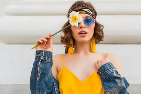 beautiful sexy woman in yellow stylish dress wearing denim jacket, holding flower, trendy outfit, hi...
