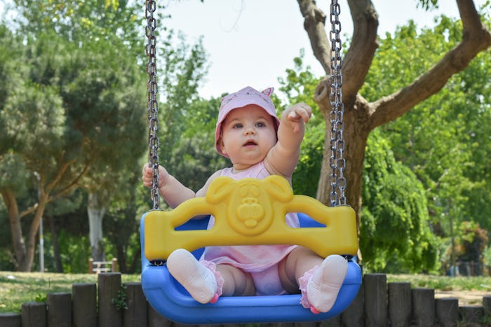 Cute adorable baby girl playing and swinging in swing in park (garden) Happy family moments concept....