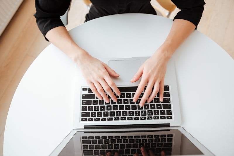 Top view photo of young lady worker sitting in office while using laptop computer and typing by keyb...