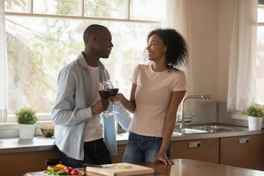 African couple in love standing in kitchen distracted from preparing dinner, diverse 30s spouses hap...