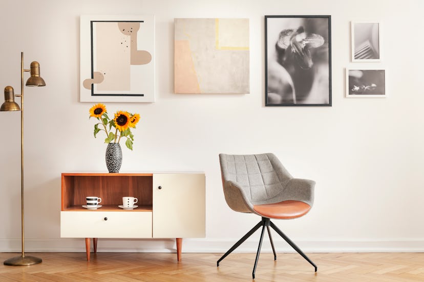 Grey armchair next to cupboard with sunflowers in white room interior with gallery. Real photo