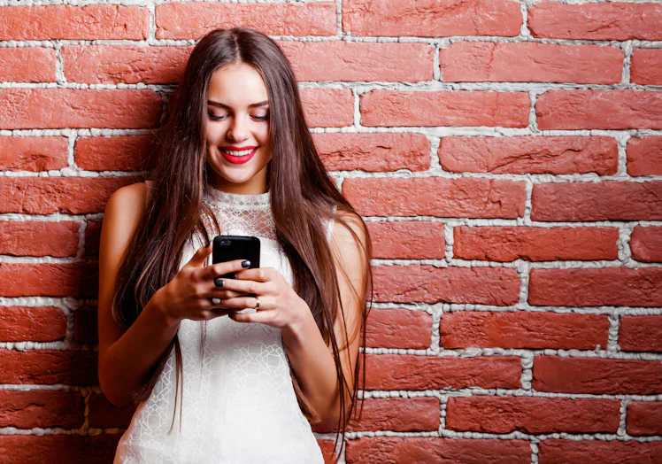 Girl texting on phone on brick wall