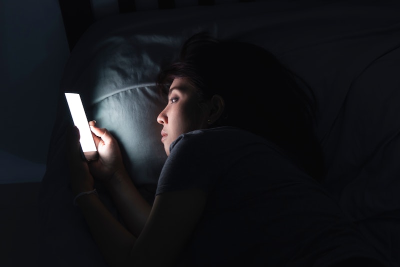 Woman using mobile phone on the bed in dark room.