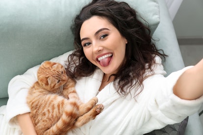 Young woman taking selfie with cute funny cat at home