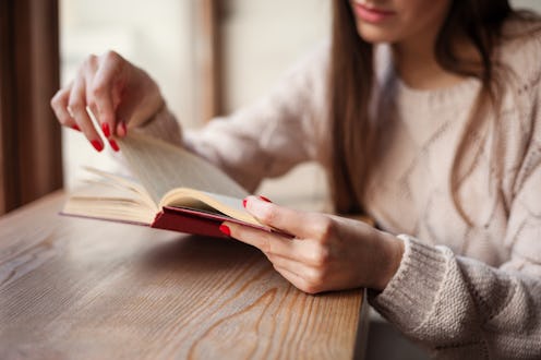 Girl holding a book wearing in warm wool pullover with red gel polish manicure. Wood retro backgroun...