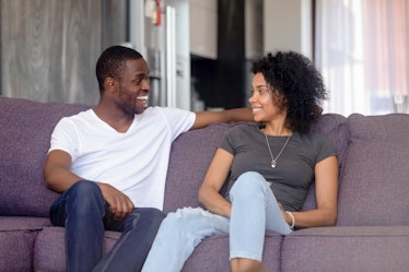 Black couple or just friends sitting on sofa in living room communicating talking at home spouses lo...