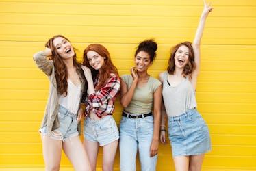 Picture of young smiling women friends standing over yellow wall. Looking at camera.