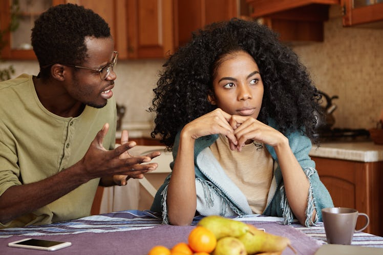 Furious black male gesturing in despair or anger while trying to make excuses to his offended wife a...