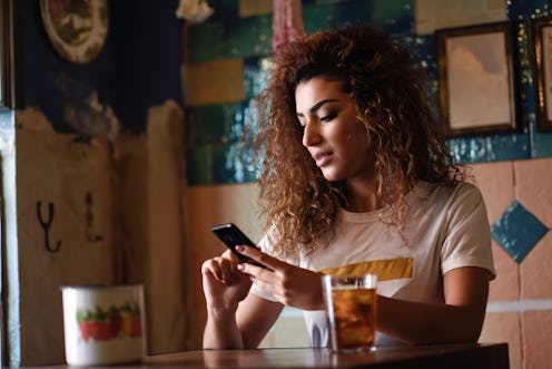 Young arabic woman with black curly hairstyle sitting in a beautiful bar with vintage decoration. Ar...