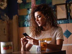 Young arabic woman with black curly hairstyle sitting in a beautiful bar with vintage decoration. Ar...