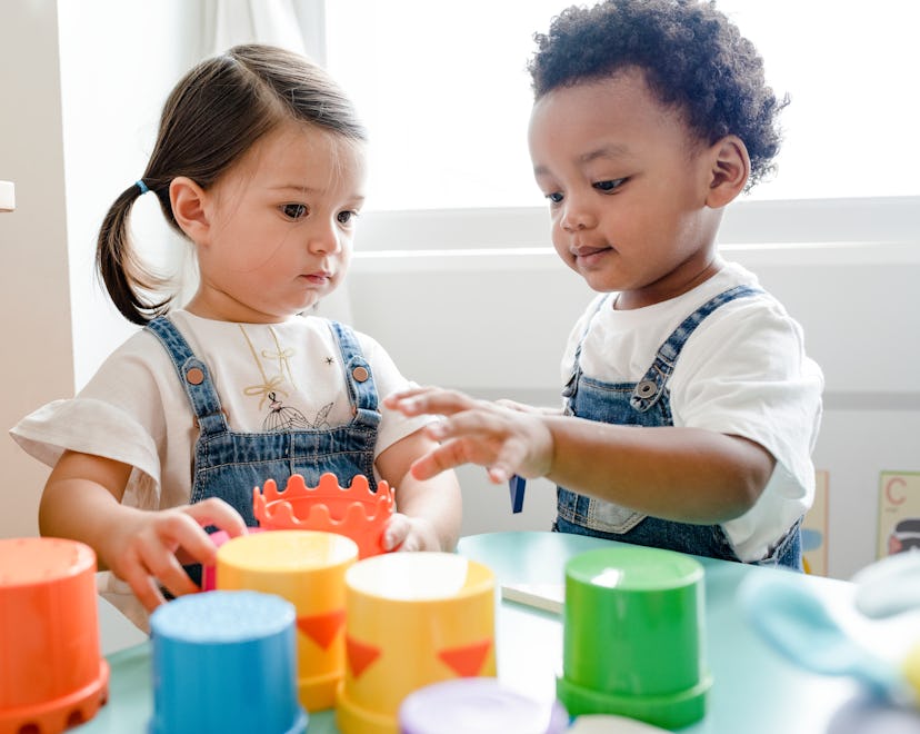 Two toddlers play together at a table with colored cups.