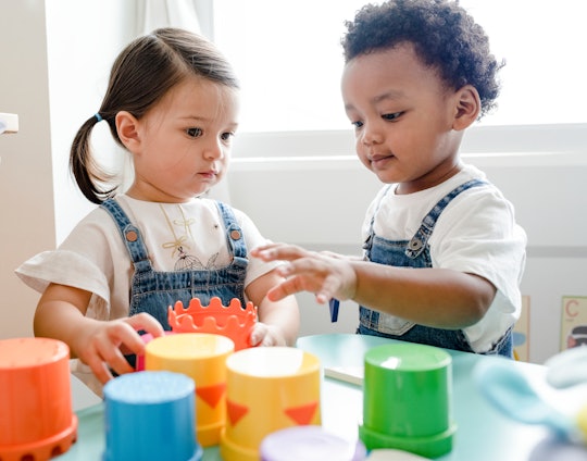 Two toddlers play together at a table with colored cups.
