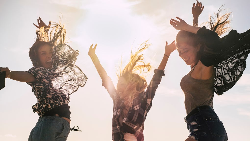 Happy young people concept youthful girls jumping and laughing together in friendship - celebration with sunlight in backlight - beautiful women and joyful
