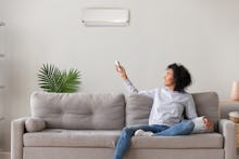 Smiling young African American woman using air conditioner, cooler system remote controller, switchi...