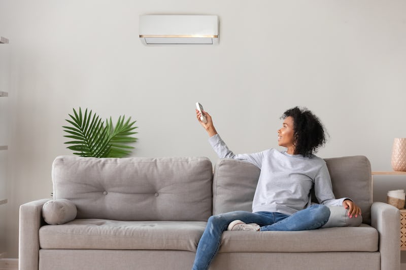 Smiling young African American woman using air conditioner, cooler system remote controller, switchi...