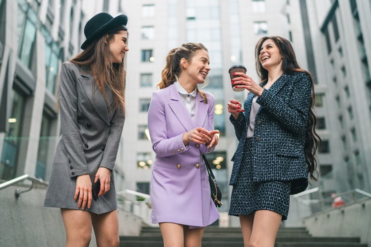 Outdoor shot of three business women in smart trendy outfit having coffee break outside the office c...