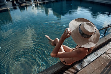 Cropped photo of Caucasian woman wearing sunhat and situating in the swimming pool. Summertime conce...
