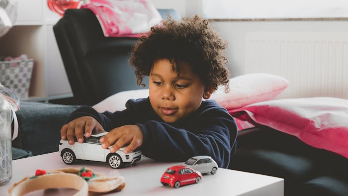 Cute 3 years old African American kid playing with toy cars at home