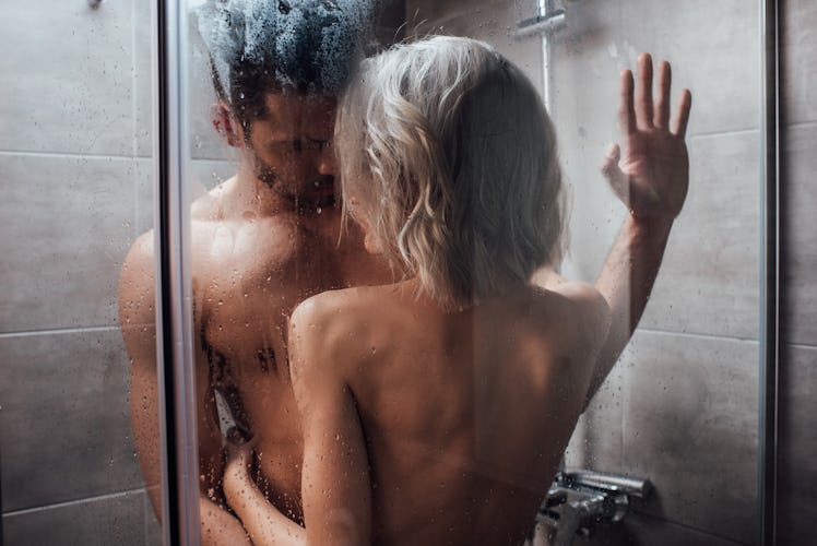 nude heterosexual couple looking at each other, embracing and taking shower together