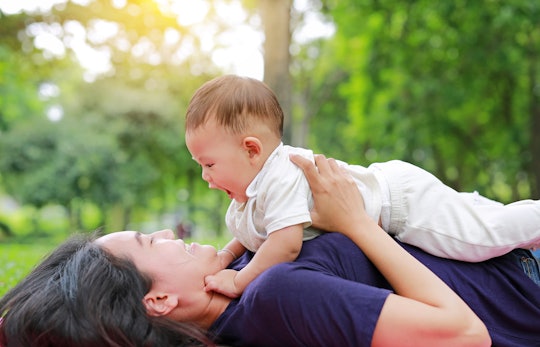 Happy Asian mom embrace her son lying in the green garden. Funny mother and infant baby boy playing ...