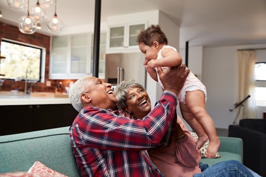 Grandparents Sitting On Sofa Playing With Baby Granddaughter At Home